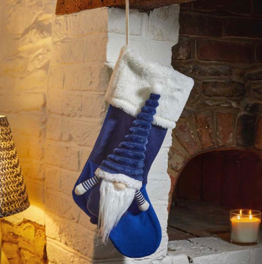A navy blue holiday stocking with a white top, hanging over a fireplace, featuring a character resembling a gnome.