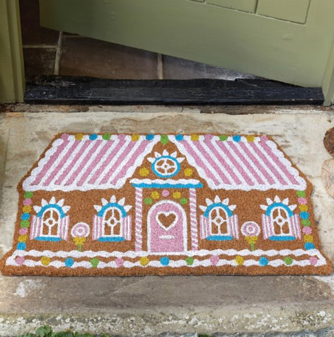 A colorful door mat featuring a gingerbread house design with intricate details and decorative elements.