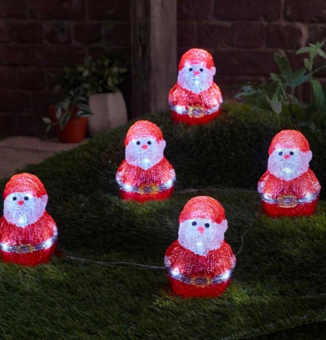 Set of five red Santa Claus figures with lights on a grassy surface.