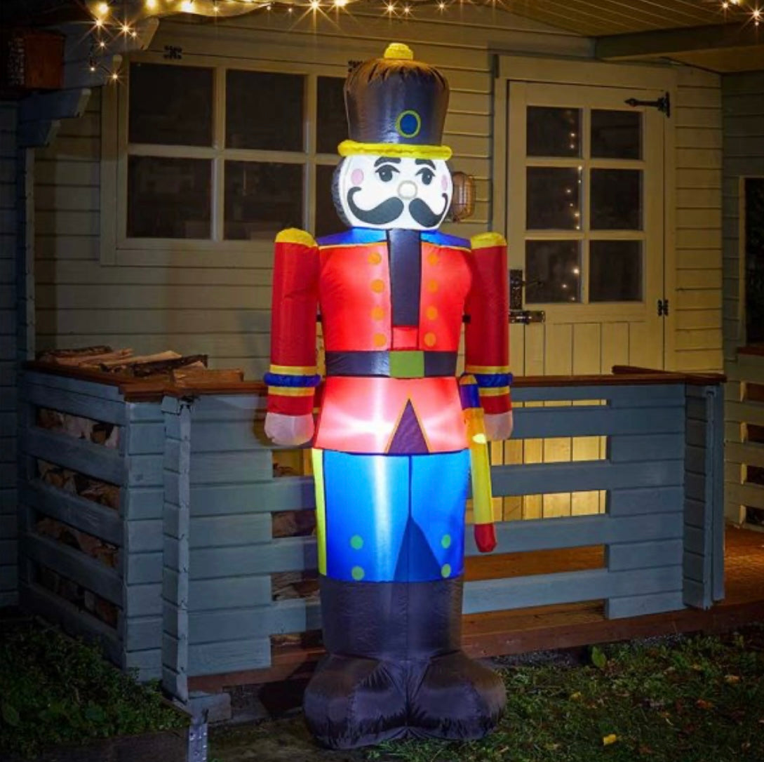 A self-inflating plastic nutcracker with multicolored clothing and a hat, featuring a Christmas-themed design, displayed on a porch.