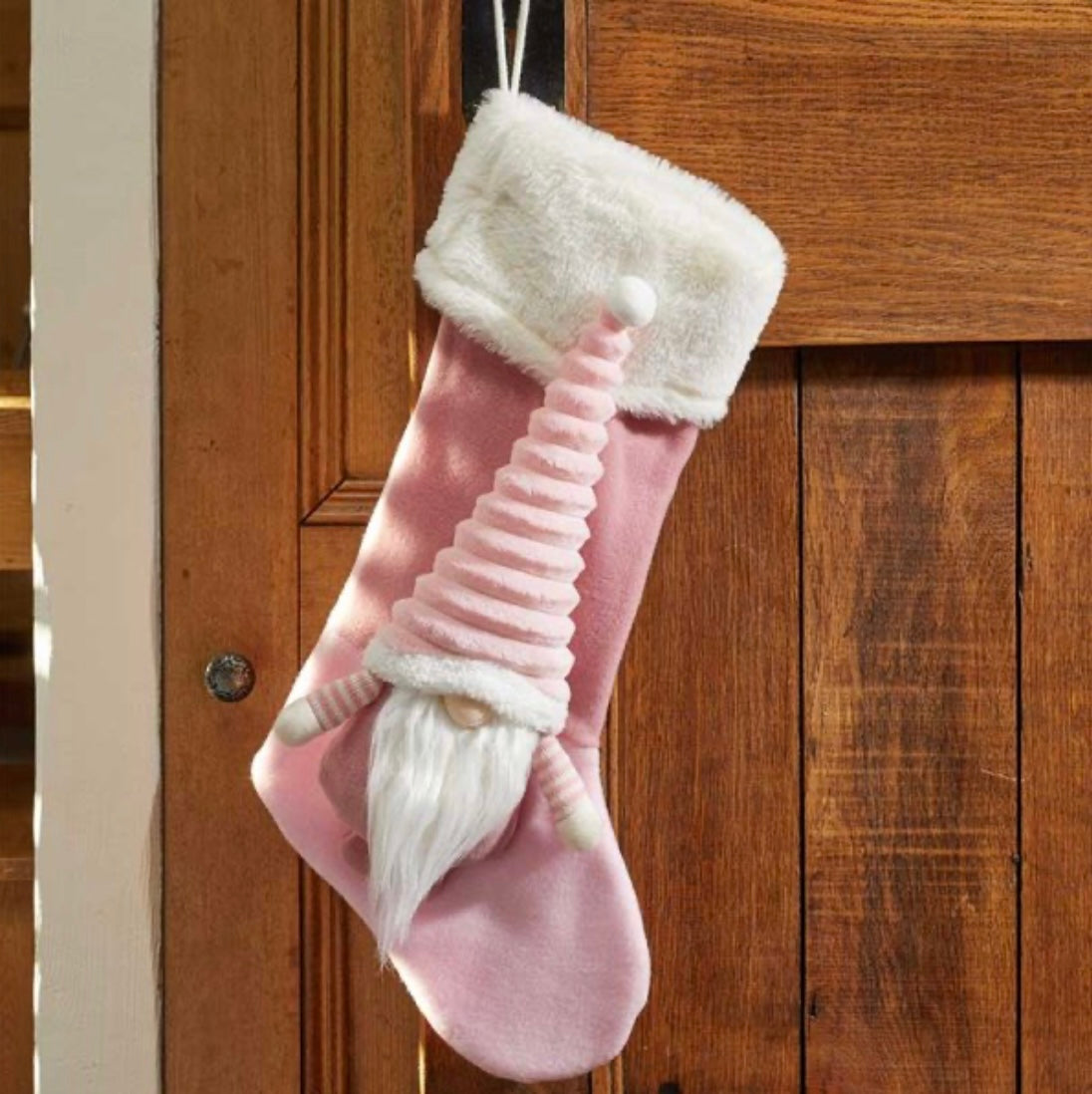 A pink holiday stocking with a white cuff and a cartoonish gnome design, hanging on a wooden door.