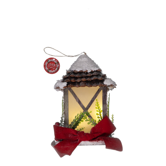 Decorative lantern ornament with a red bow and snow on top, on a white background.
