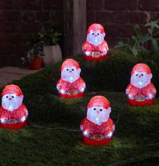 Set of five red Santa Claus figures with lights on a grassy surface.
