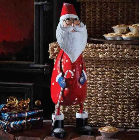 A decorative Santa figurine with a red outfit, white beard and hair, wearing glasses, and a blue mitten. The figure is standing next to a wicker basket with a pie inside.